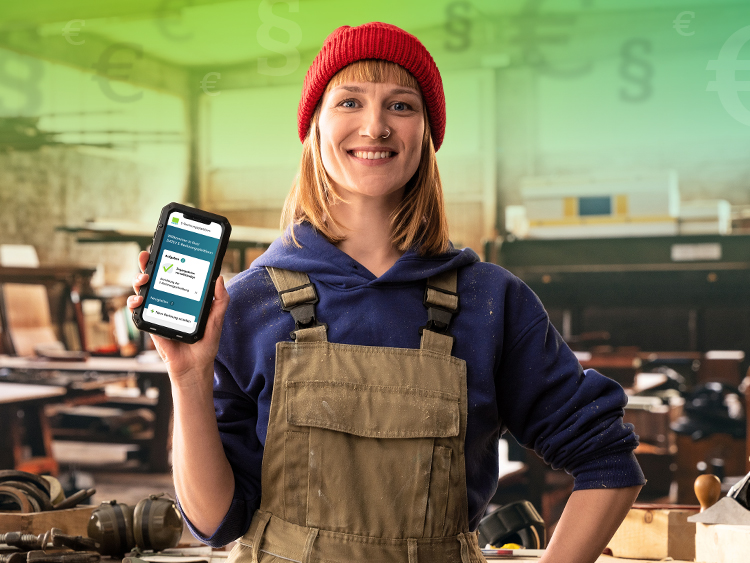 Fröhliche junge Frau mit Arbeitskleidung in einer Schreinerei hält ein Smartphone nach vorne, auf dem die DATEV E-Rechnungsplattform zu sehen ist